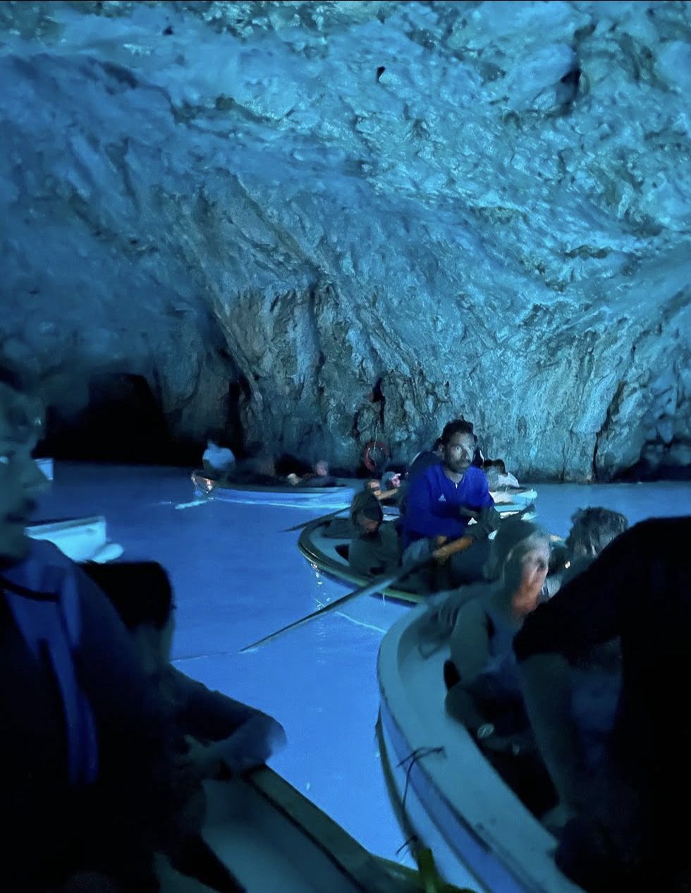 Wooden rowboat oarsman guiding tourists through the narrow cave entrance of the Blue Grotto on Capri